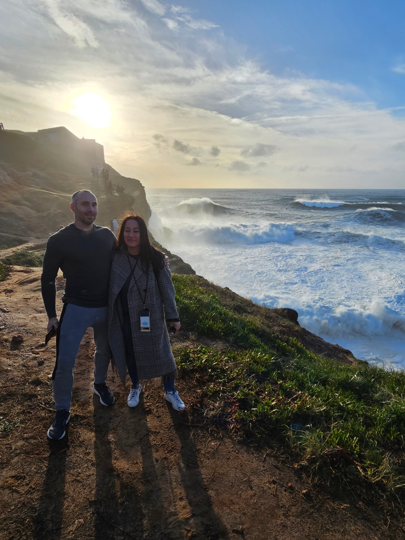 Couple on the Praia do Norte cliffs as Atlantic waves crash below
